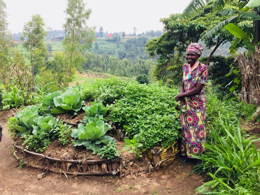 HIV+ widow in Muhanga district standing proudly in front of her kitchen garden which was funded by SEP